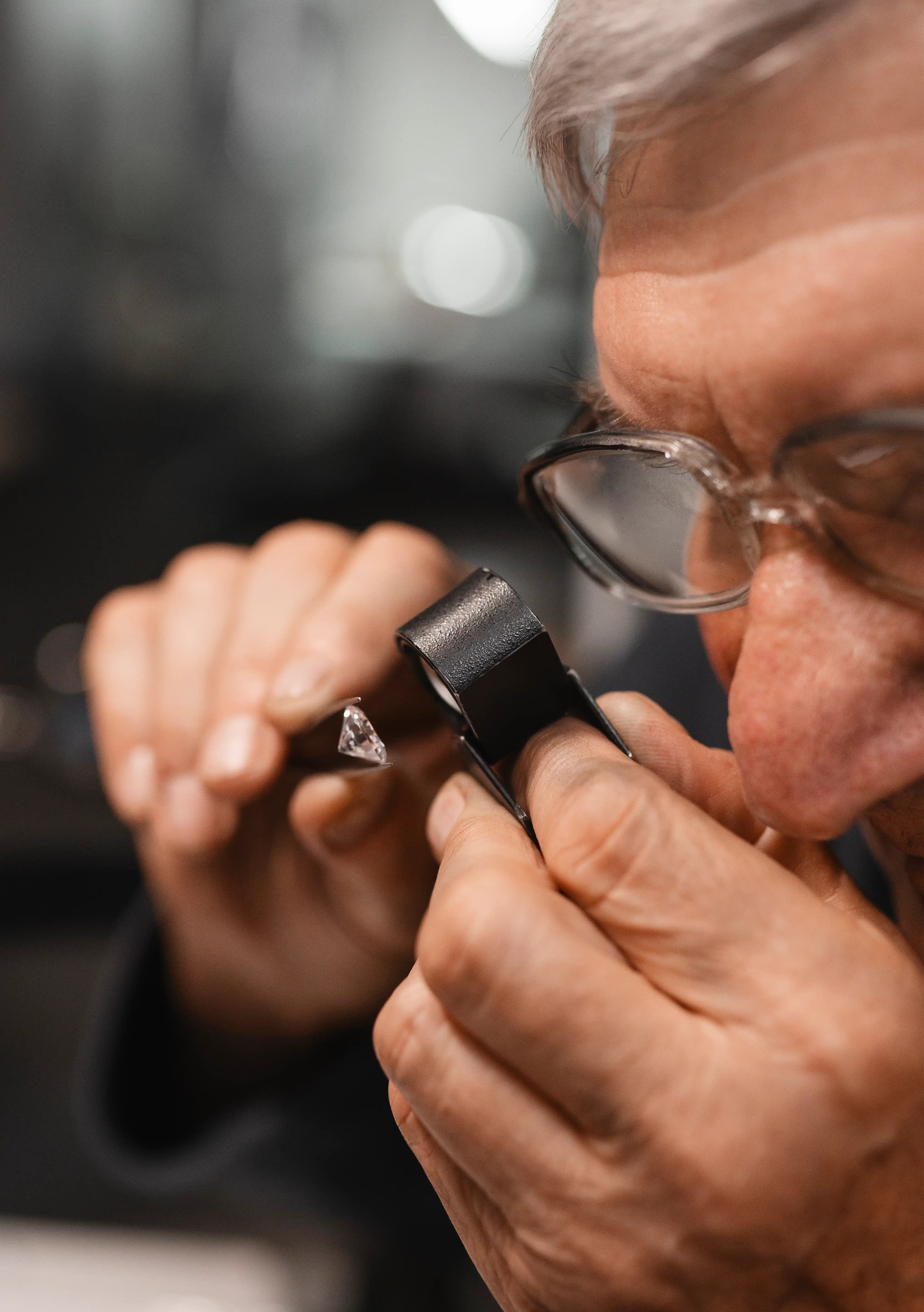 Jewelry expert examining loose lab created diamond with magnifying loupe for quality and clarity grading.